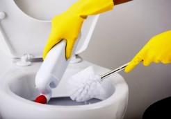 Female hand in yellow rubber glove is cleaning toilet bowl using brush.